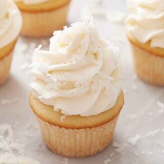 Multiple cupcakes topped with coconut frosting and shredded coconut.