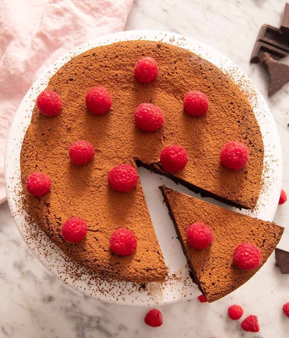 Overhead view of a flourless chocolate cake topped with raspberries with a slice cut out and pulled out.