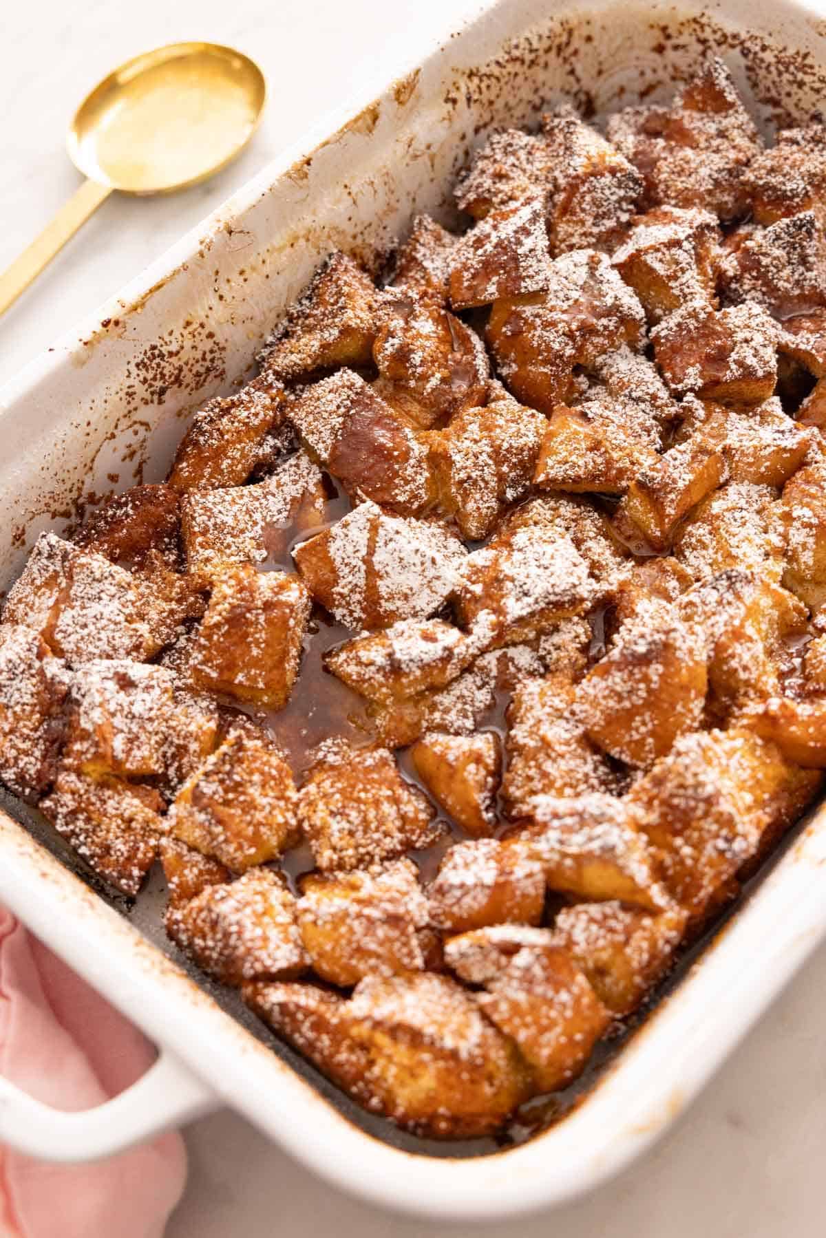 A white baking dish containing a French toast casserole. A serving spoon in the background.