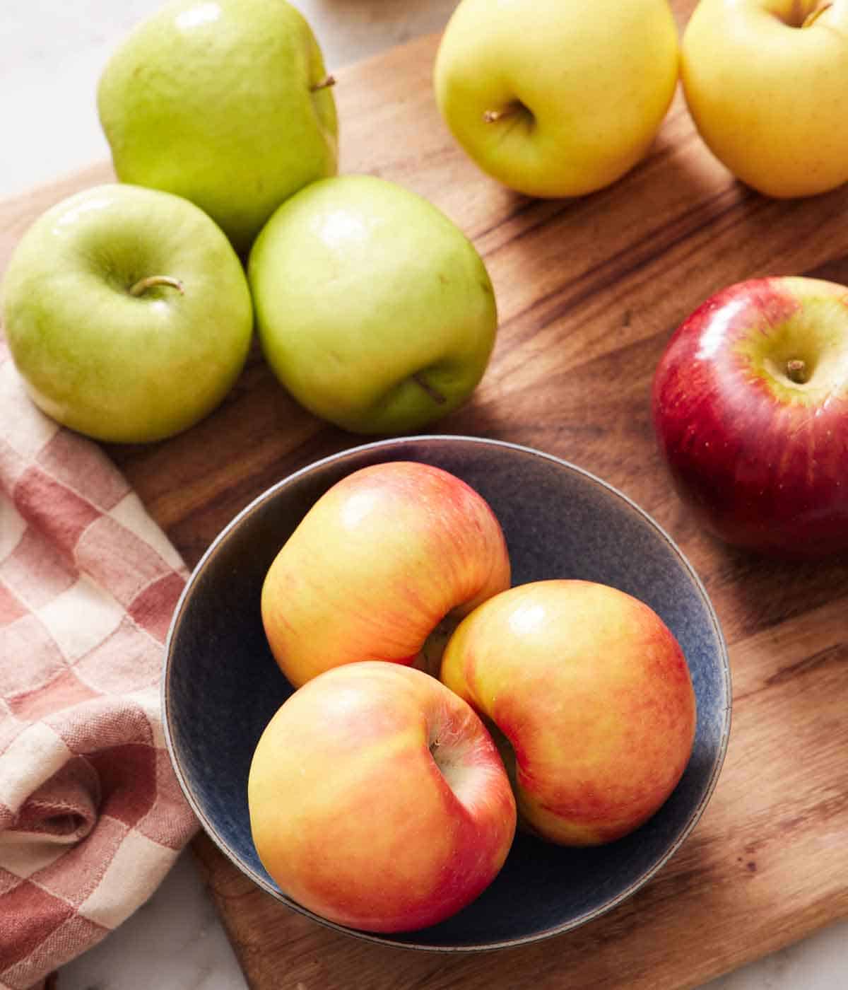 Apples on a cutting board and in a bowl on the board.