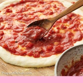 Pinterest graphic of a spoon adding pizza sauce to stretched pizza dough.