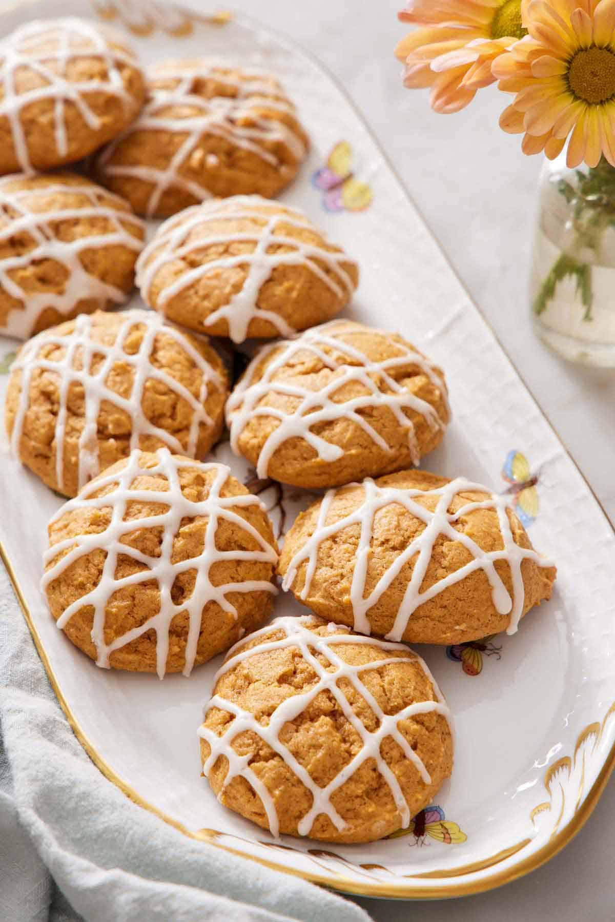 A platter of pumpkin cookies with icing drizzled on top. Yellow flowers off to the side.