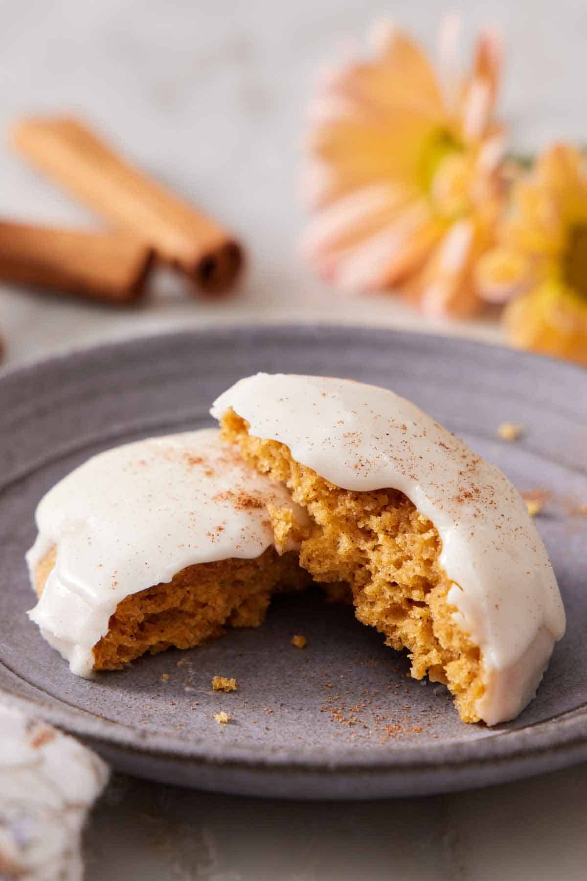 A plate with a pumpkin cookie covered with icing, torn in half, with one half leaning on top of the other.