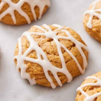 Multiple pumpkin cookies with icing drizzled on top.