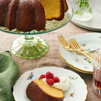 Pinterest graphic of a slice of rum cake on a plate with whipped cream and raspberries. The rest of the cake on a cake stand behind it.