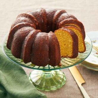 A cake stand with a rum cake with two pieces sliced. Stack of plates and forks beside it.