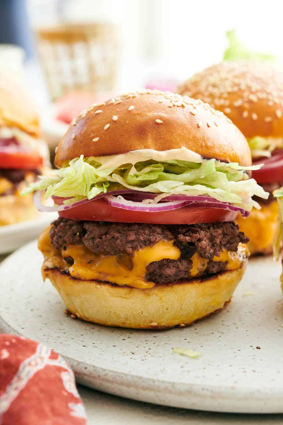 A profile view of a smash burger topped with tomato, onion, and lettuce.