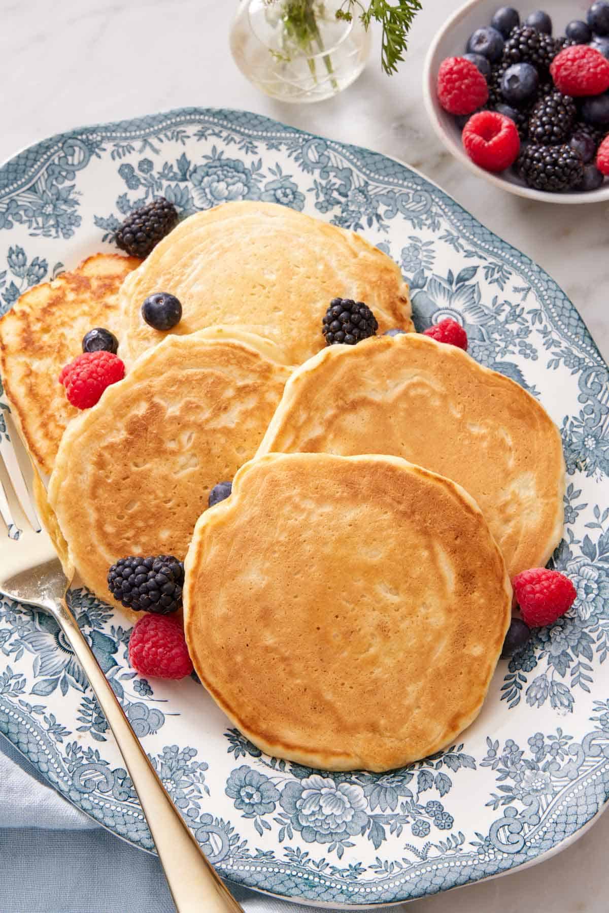 A platter of sourdough pancakes with fresh berries scattered around. A small bowl of berries in the background.