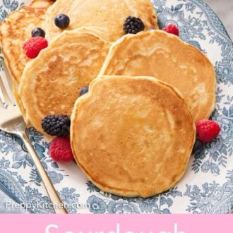 Pinterest graphic of a blue and white platter of sourdough pancakes with fresh berries scattered around.