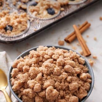 Pinterest graphic of a bowl of streusel topping with cinnamon sticks and muffins topped with streusel in the background.