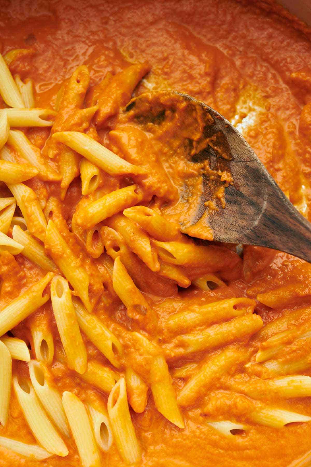 A close up view of cooked pasta tossed in vodka sauce with a wooden spoon.