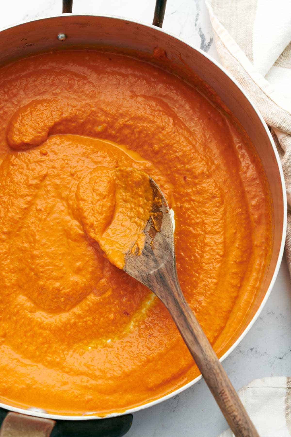 Overhead view of a pot of vodka sauce being turned by a wooden spoon.