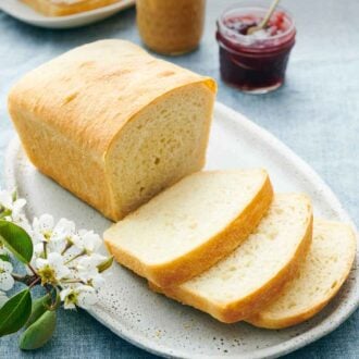 Pinterest graphic of a platter with a loaf of white bread with three slices cut in front. Peanut butter and jam in the background.