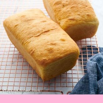 Pinterest graphic of two loaves of white bread on a copper cooling rack with a blue linen napkin beside it.