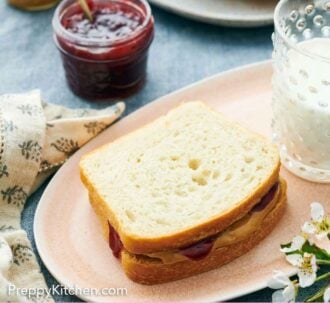 Pinterest graphic of a platter with a peanut butter and jam sandwich made with white bread. Jam in the background along with a drink and sliced bread.