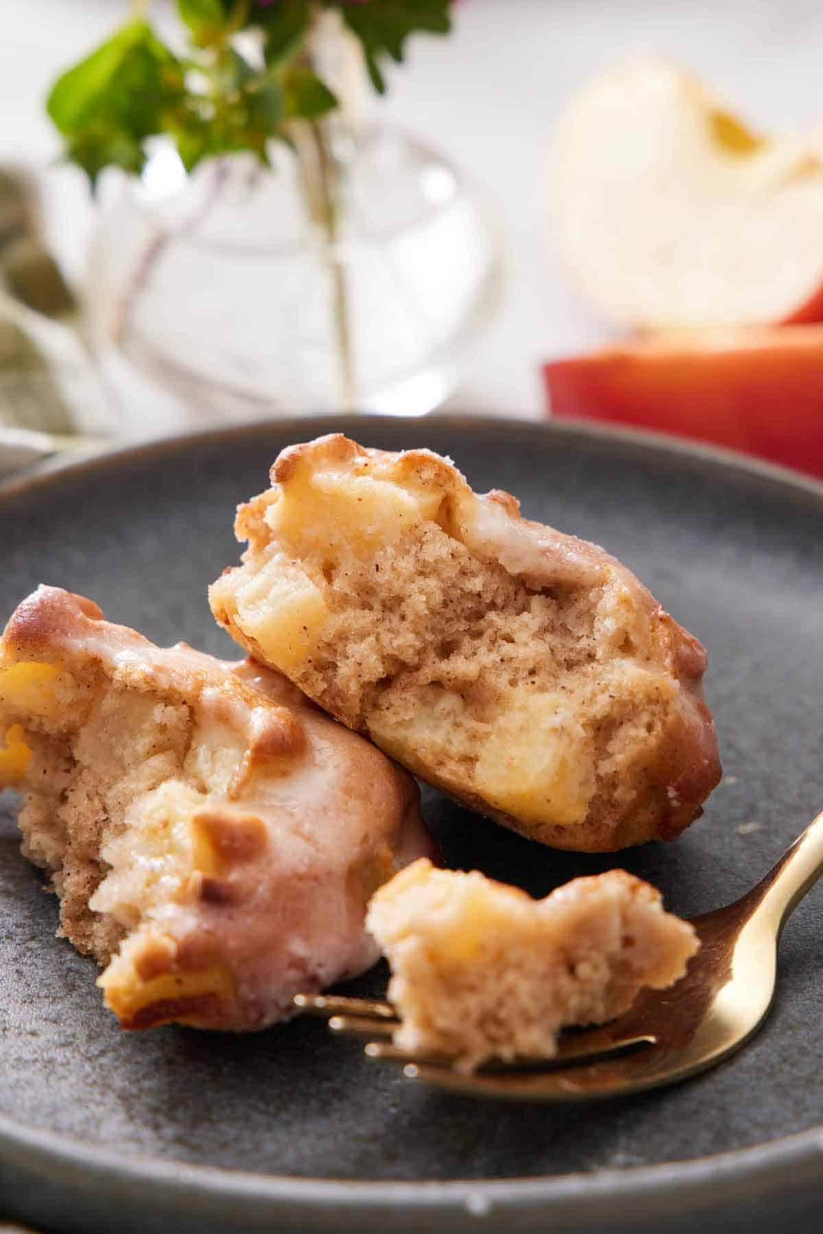 A close up view of an air fryer apple fritter on a plate, cut in half, with a small bite on the fork in front.