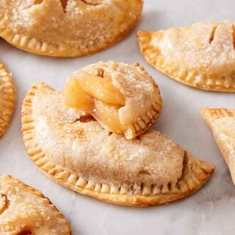 Multiple air fryer hand pies on a marble surface with a cut on leaning on top of the middle pie, showing the interior.