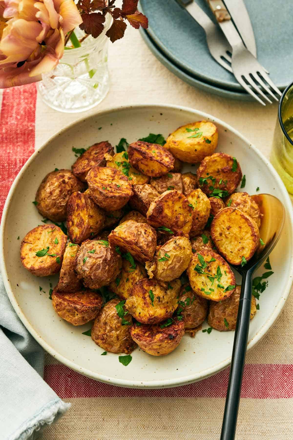 Overhead view of air fryer potatoes in a plate with a spoon. Flowers, forks, and plates on the side.