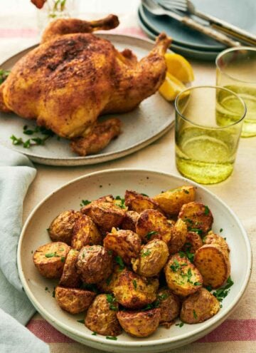 A plate with air fryer potatoes with two drinks in the back along with a whole roast chicken.