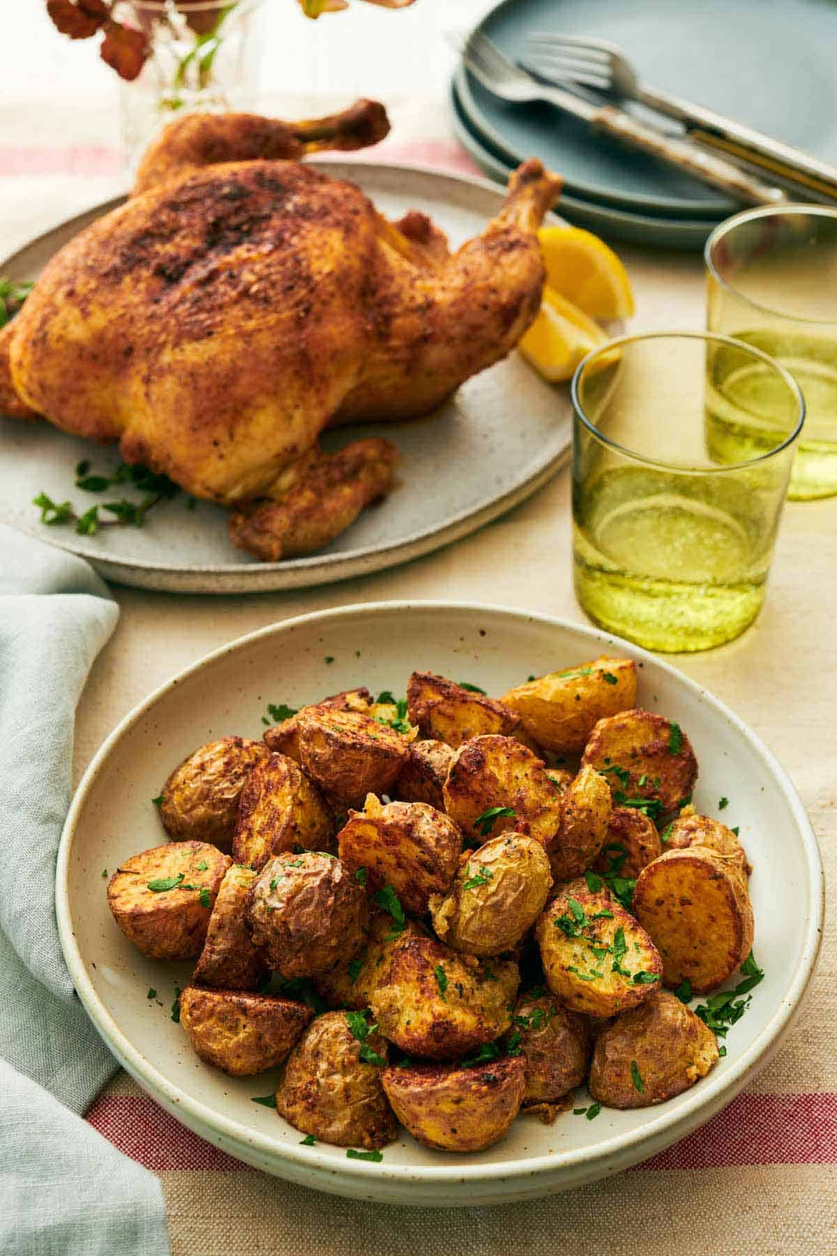 A plate with air fryer potatoes with two drinks in the back along with a whole roast chicken.