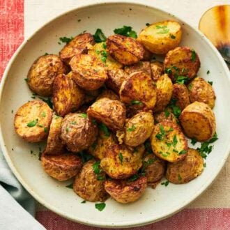 A plate with air fryer potatoes with chopped parsley on top with a spoon on the side.