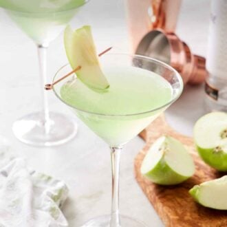 Pinterest graphic of glasses of apple martini with sliced apple garnishes. Cut apples and a cocktail shaker on the side.