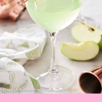 Pinterest graphic of an apple martini with a jigger, cut apples, cocktail shaker, and linen napkin on the side.