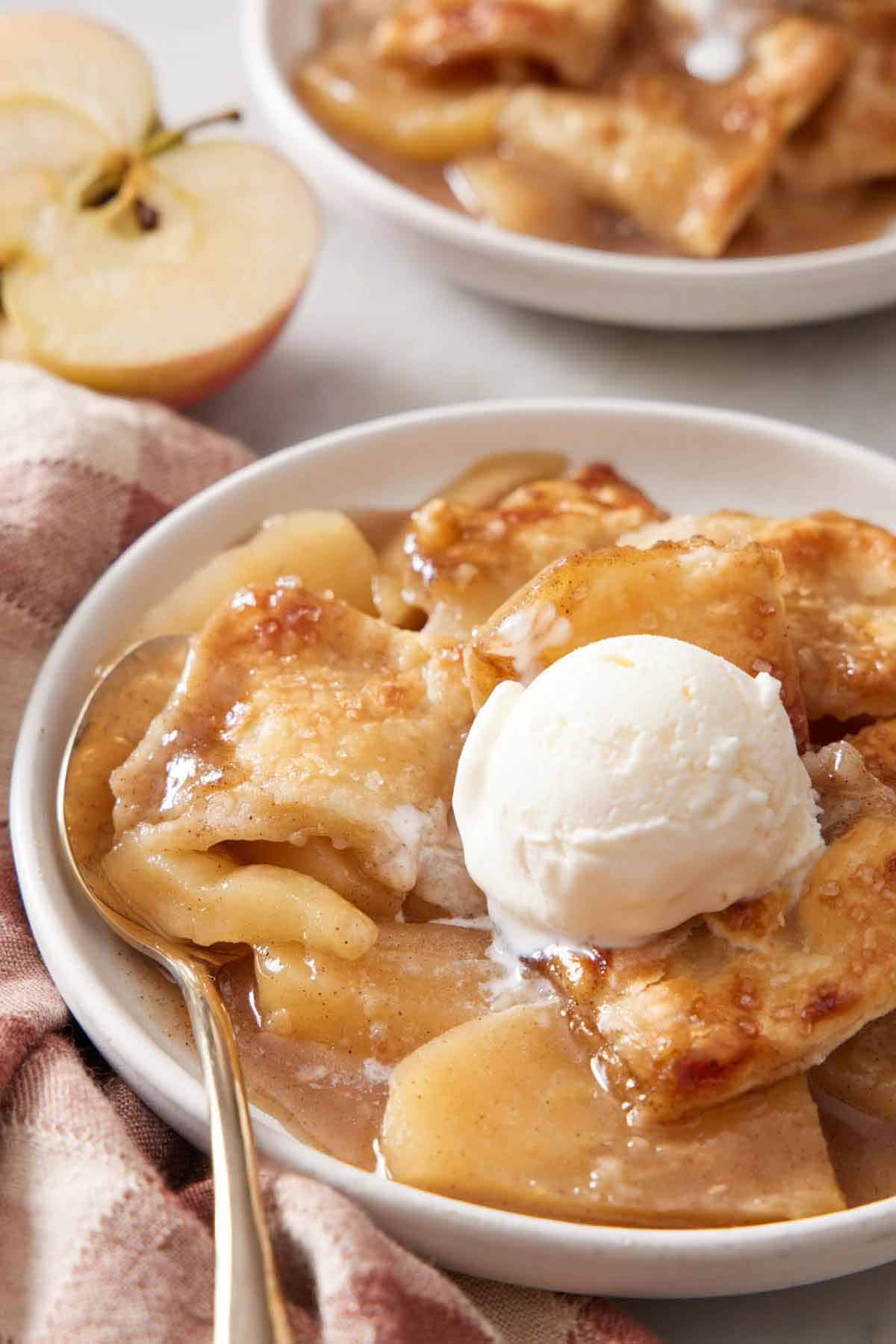 A plate with apple pandowdy with a scoop of vanilla ice cream with a spoon.