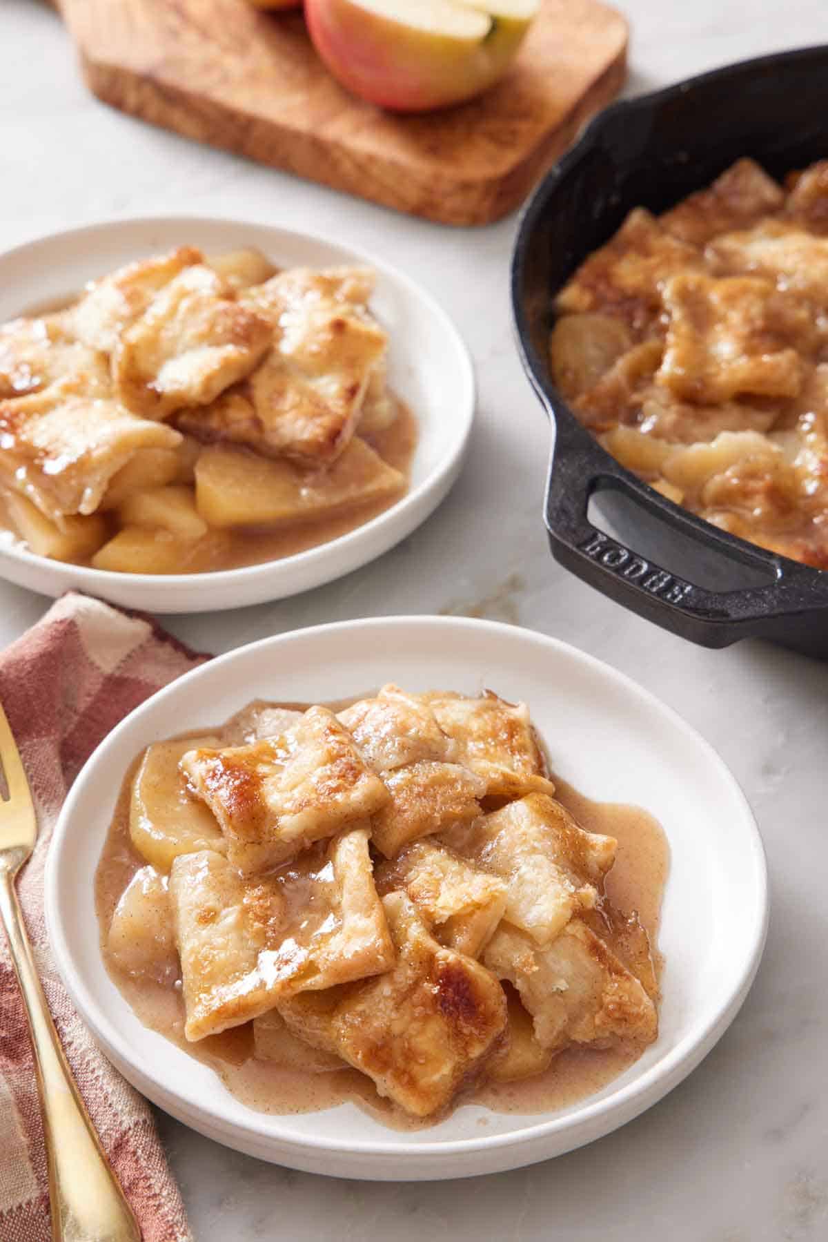 Two plates of apple pandowdy with a skillet on the side.