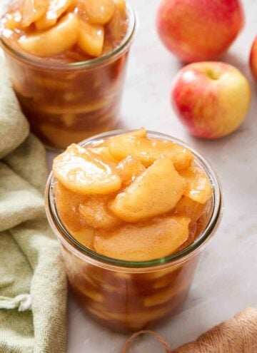 Two jars of apple pie filling. A linen napkin and a couple of apples on the side.