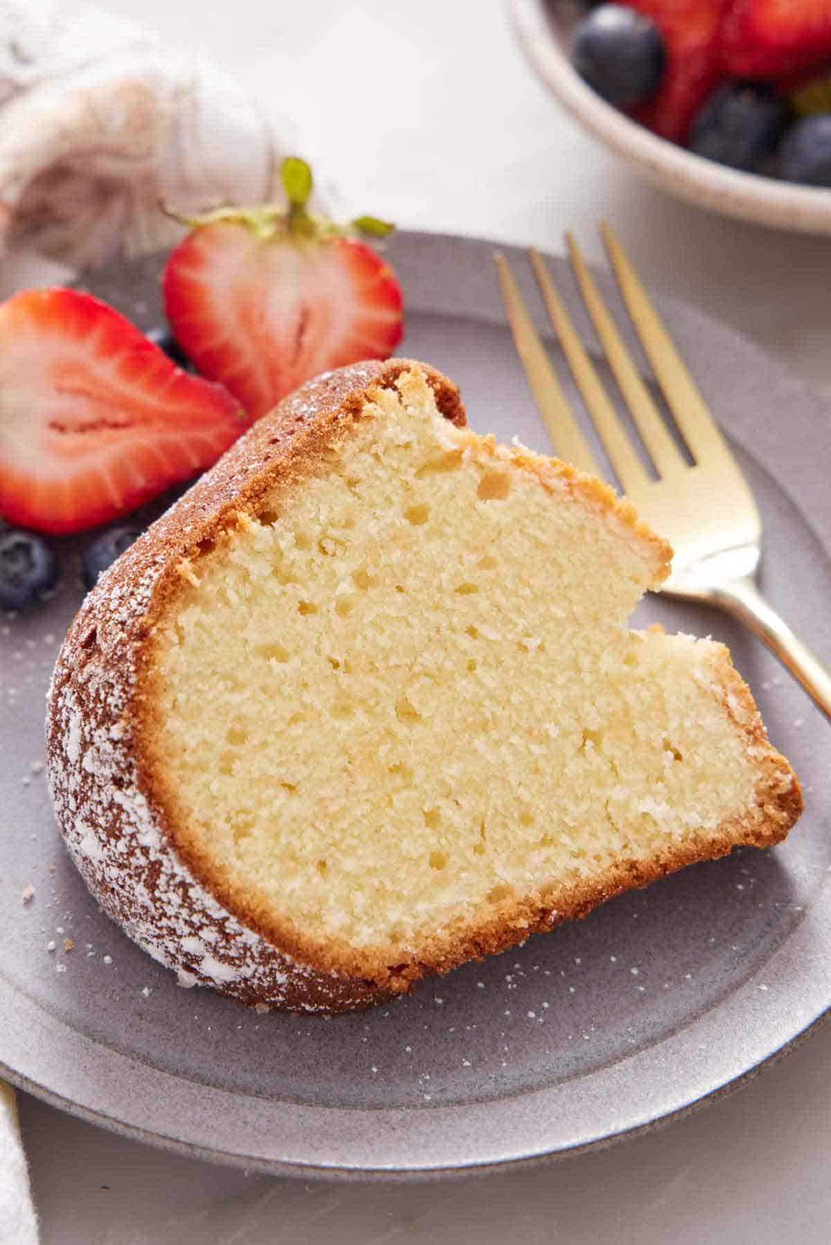 A close up view of a slice of cream cheese pound cake on a plate with a fork and some berries.