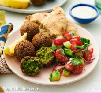 Pinterest graphic of a plate with four falafel, with one cut in half. Pita bread, cucumbers, tomatoes, and a lemon wedge on the plate as well. A bowl of tahini sauce in the back.