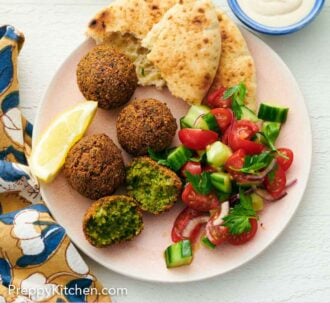 Pinterest graphic of a plate with multiple falafel with one torn opened. Pita bread, lemon wedges, and cucumber-tomato salad on the plate too.