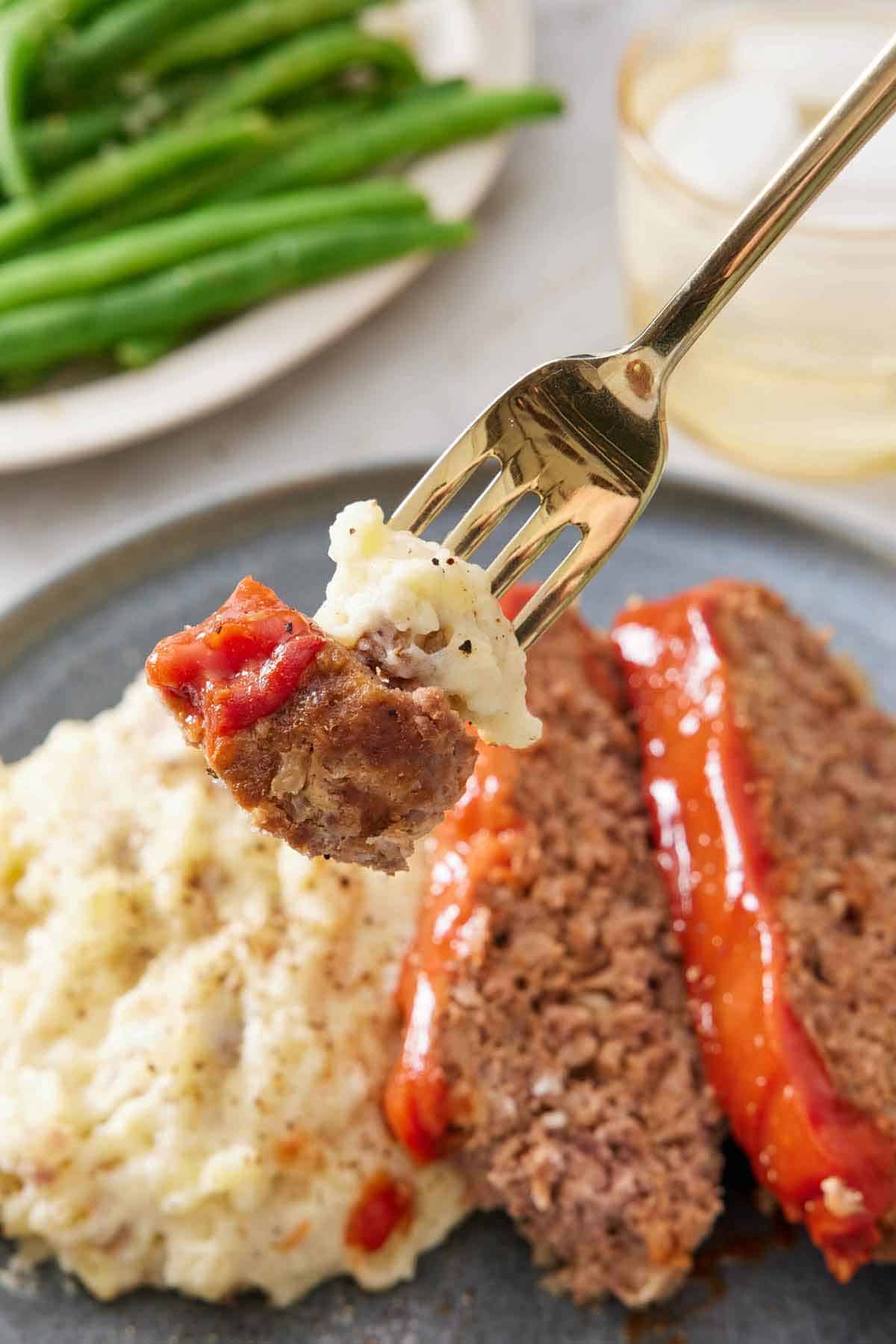 A fork lifting up a bite of Instant Pot meatloaf and mashed potatoes from a plated serving.