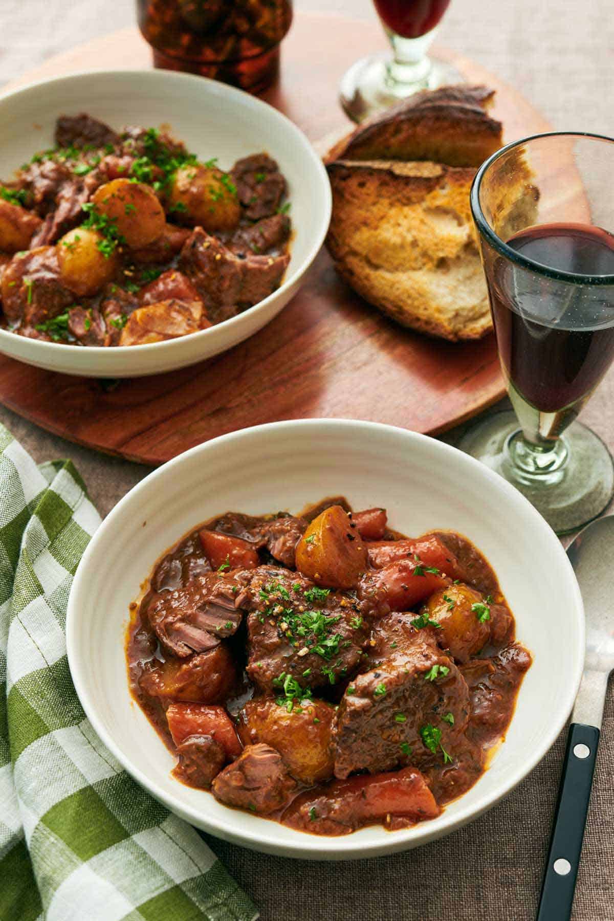 Two bowls of lamb stew with a glass of red wine and some torn bread.