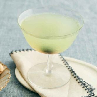 A glass of Last Word Cocktail on a napkin on a platter with a bowl of pistachio on the side.