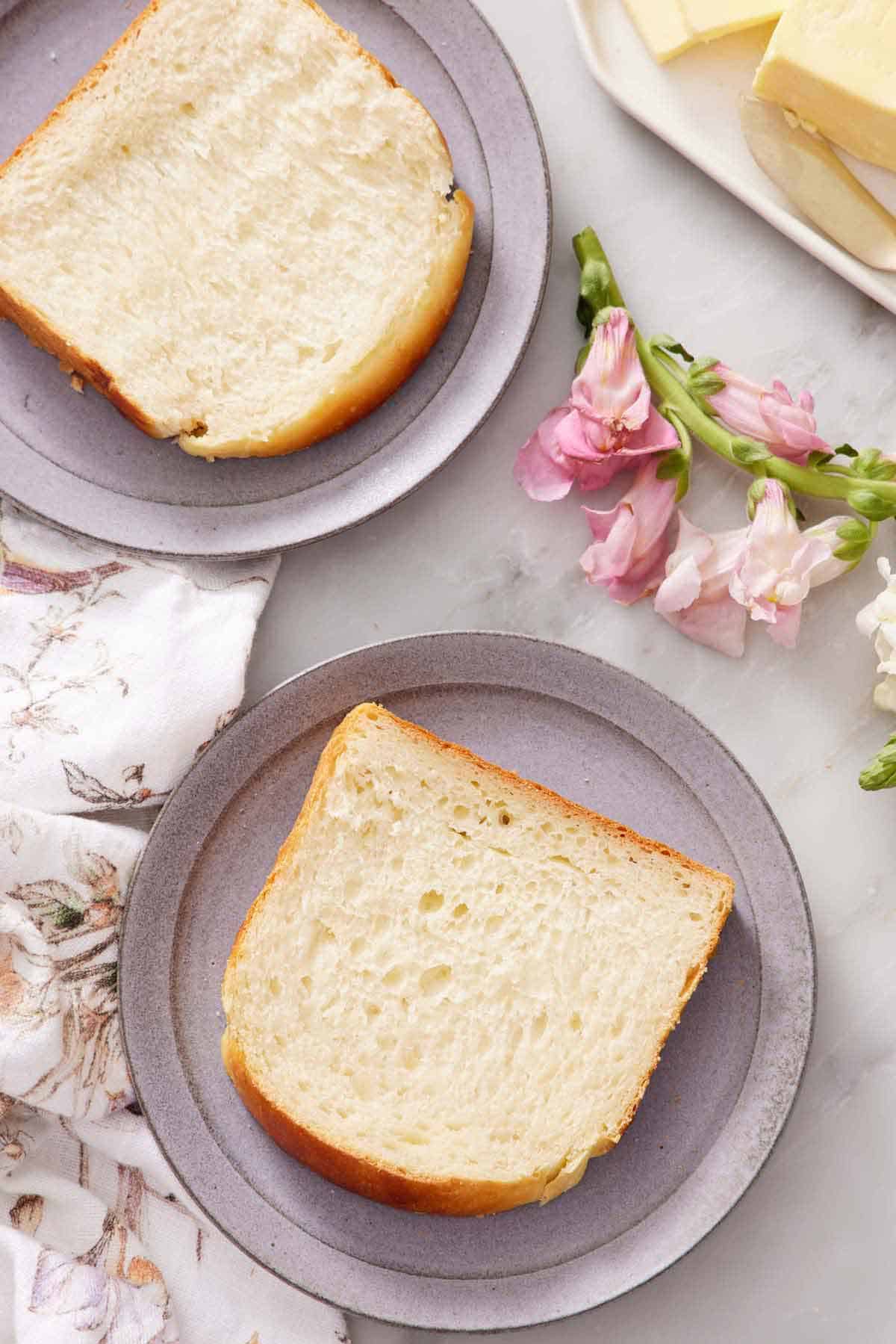 Overhead view of two plates with a slice of milk bread each. Flowers and butter on the side.