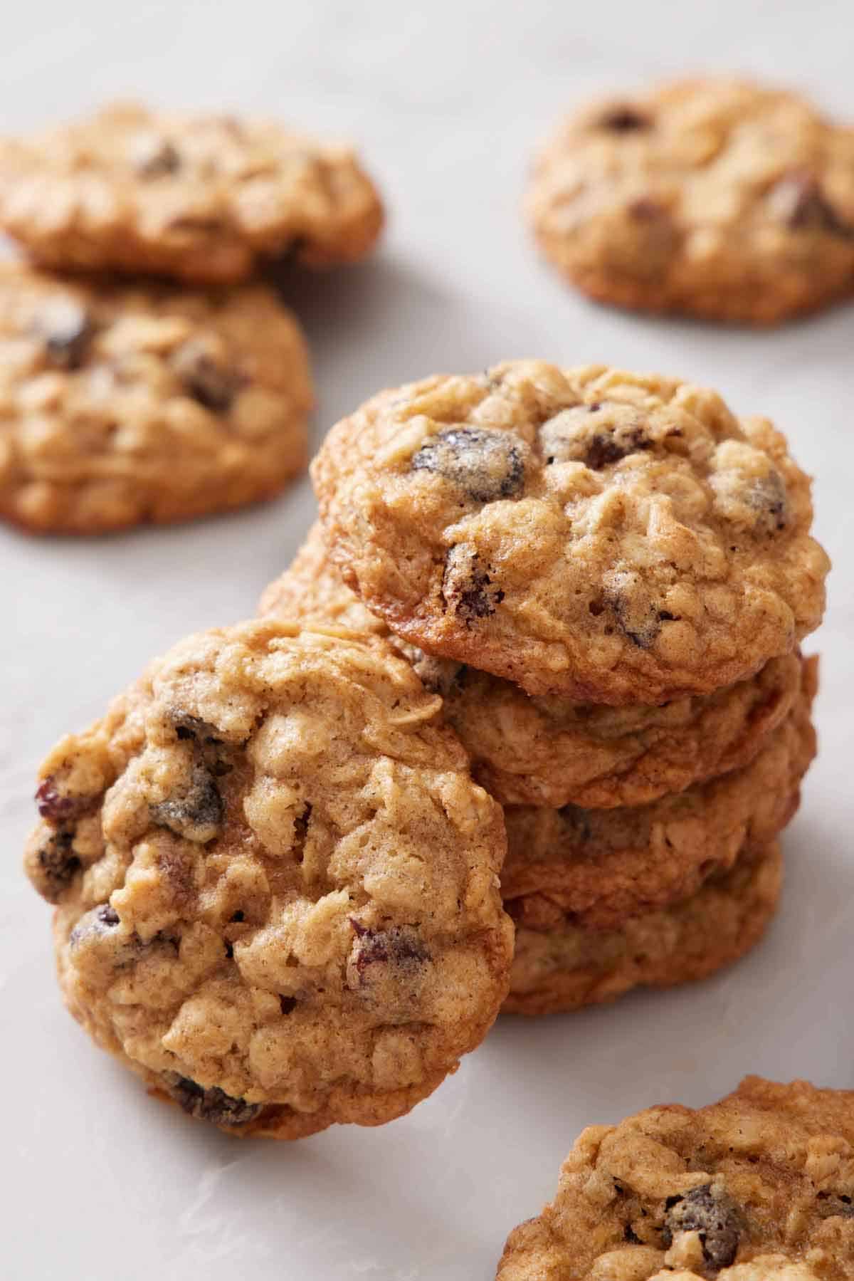 A stack of four oatmeal cookies with one leaning beside it. More cookies scattered around.