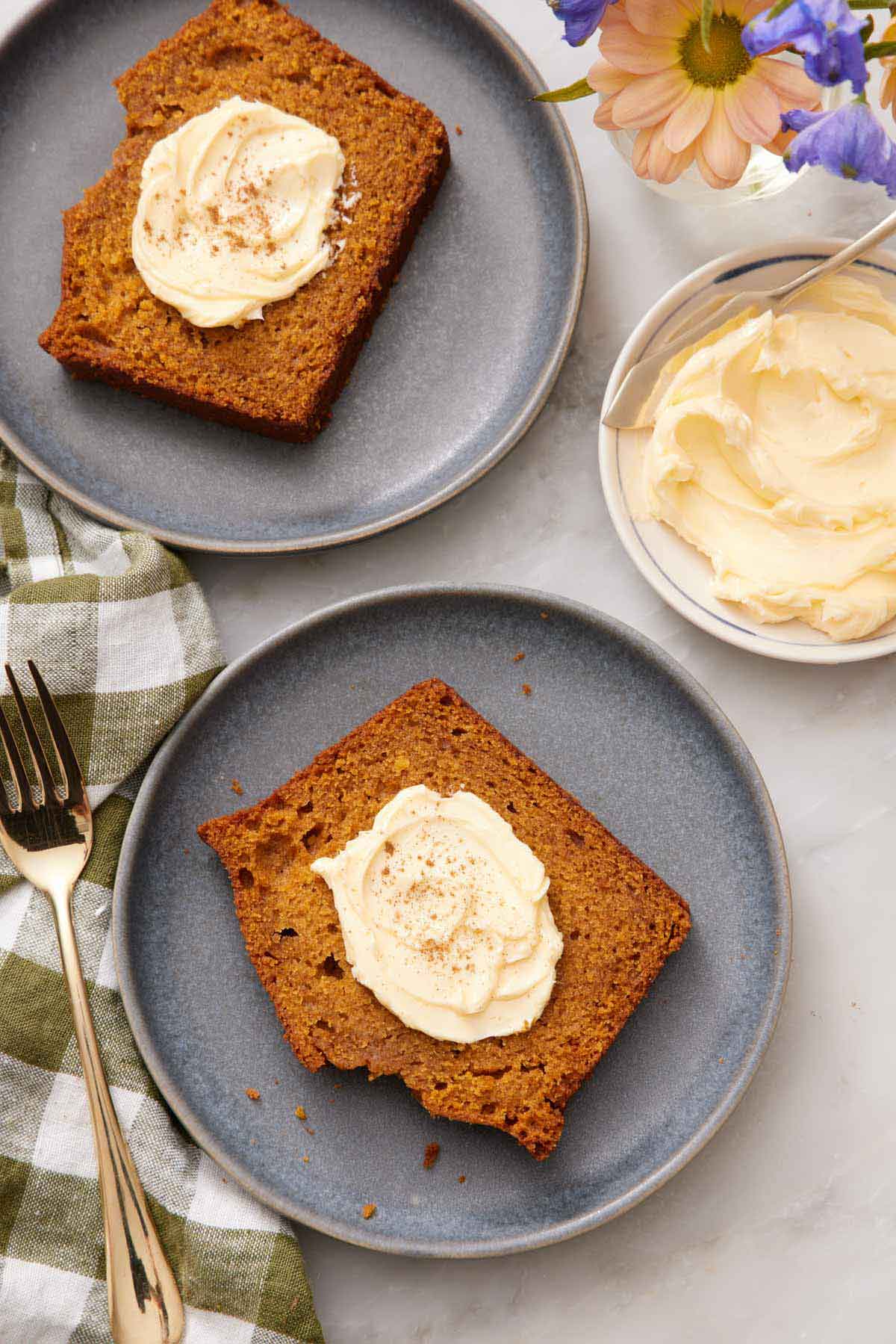 Overhead view of two slices of pumpkin bread on separate plates, topped with butter.