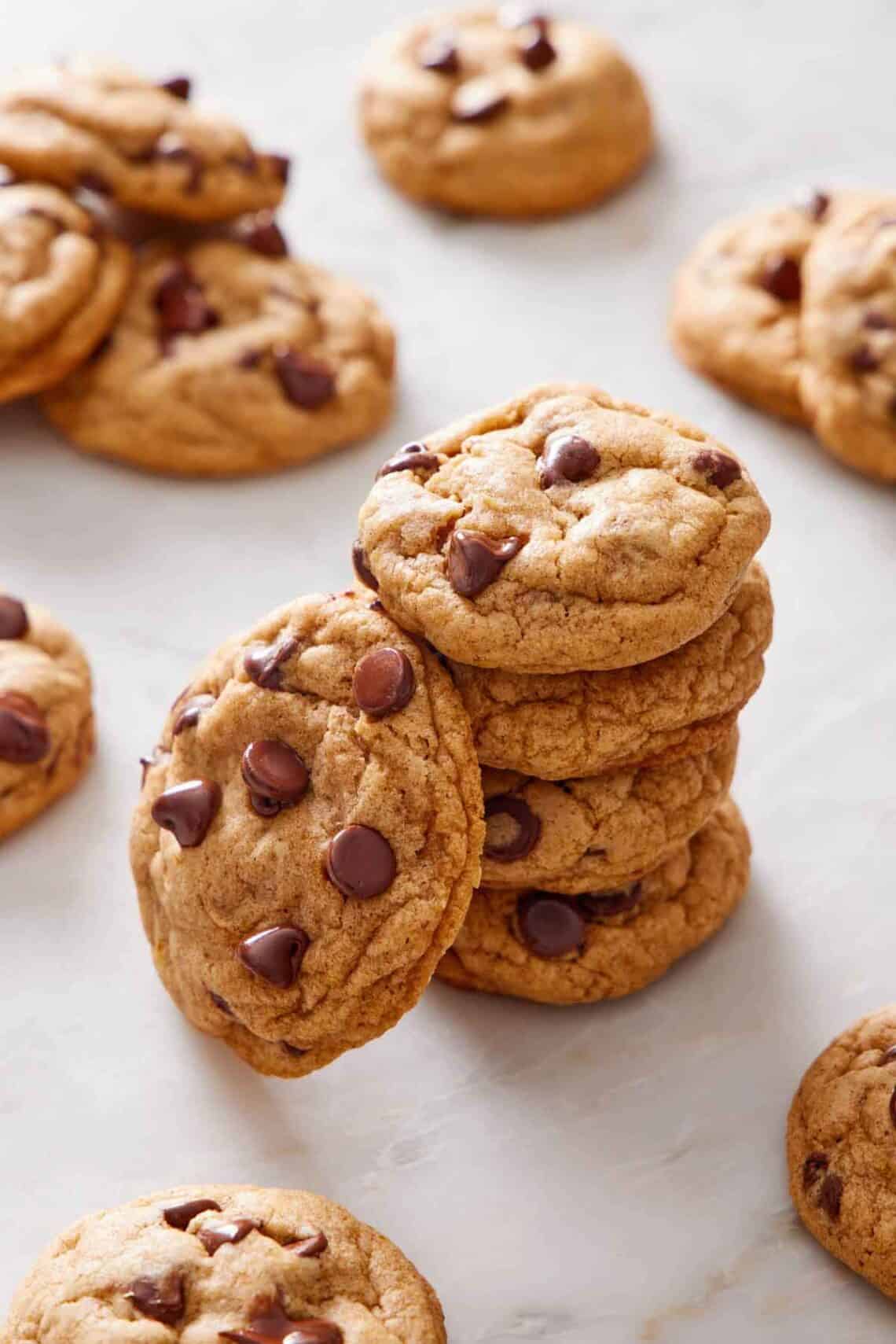 A stack of pumpkin chocolate chip cookies on a marble surface with more cookies scattered around.