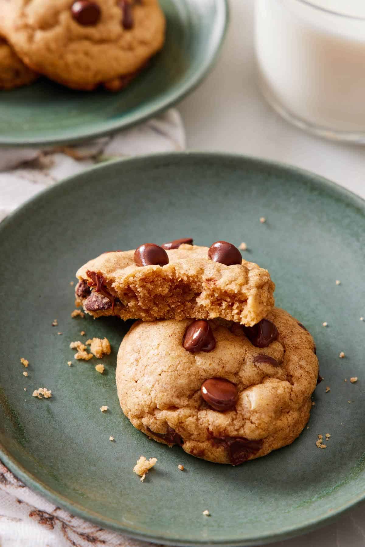 A green plate with two pumpkin chocolate chip cookies, one on placed on top, half eaten.