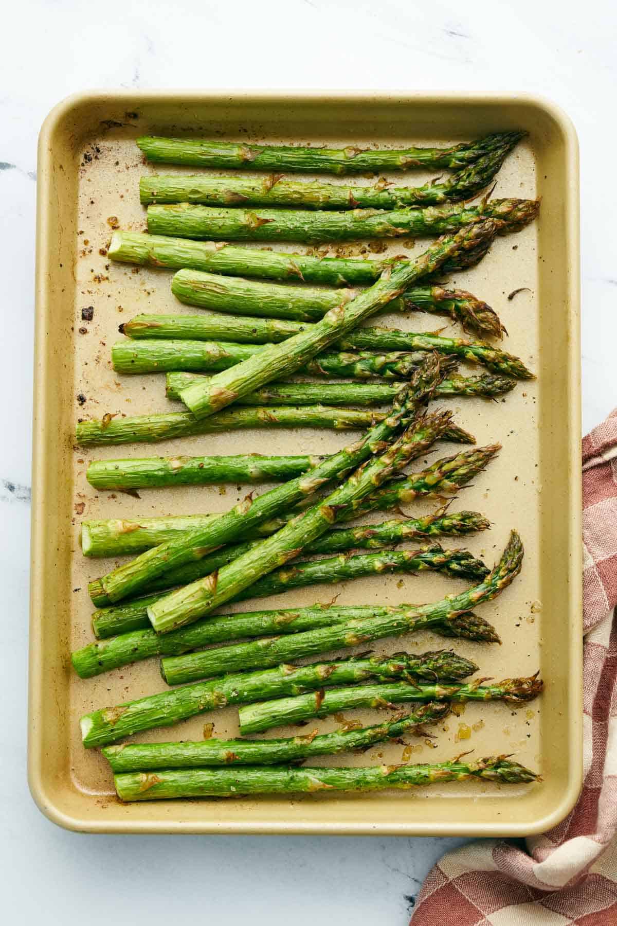 Overhead view of a sheet pan with roasted asparagus. A linen napkin on the side.