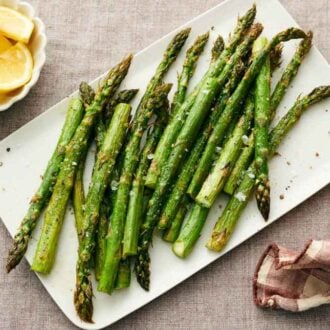 A platter of roasted asparagus with a bowl of lemon wedges and a linen napkin beside it