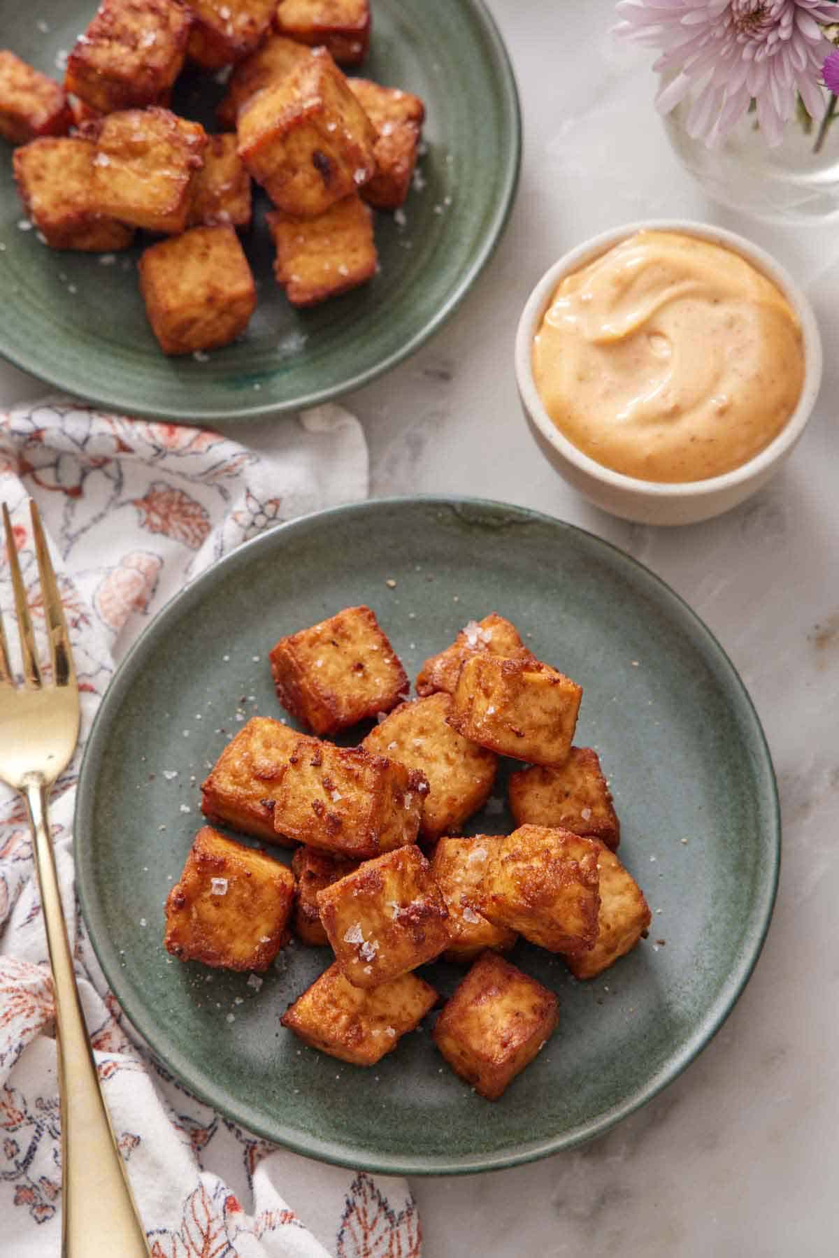 Overhead view of two plates of air fryer tofu with a bowl of dipping sauce on the side.