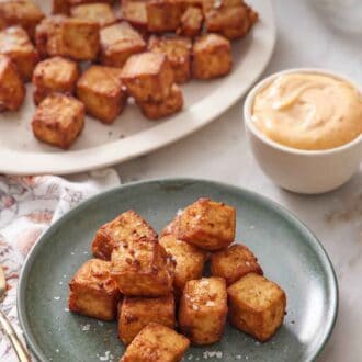 Pinterest graphic of a plate with a pile of air fryer tofu with a platter in the background with more tofu. A bowl of dipping sauce on the side.