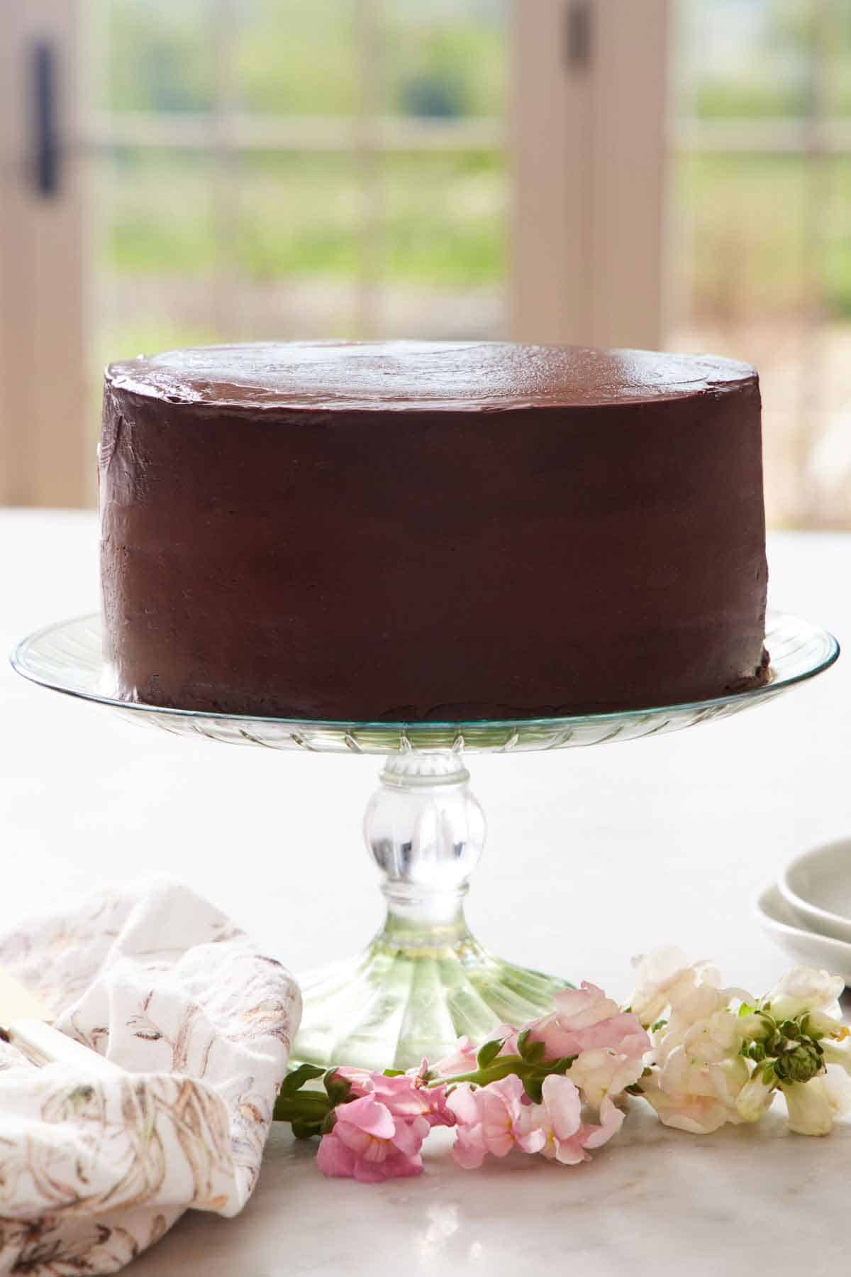 A clear cake stand holding a Ding Dong cake. A linen napkin and flowers in front.