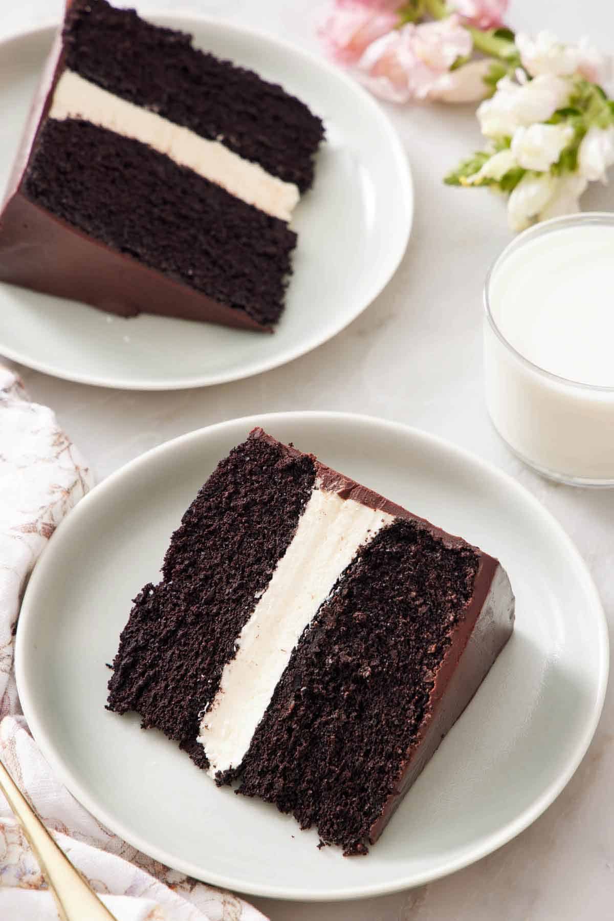 Two plated slices of Ding Dong cake on their sides. A glass of milk and flowers off to the side.