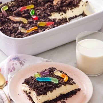 A plate with a slice of dirt cake with a glass of milk and rest of the cake in the background.