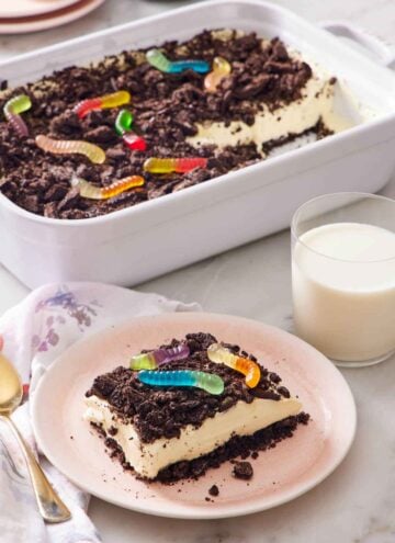 A plate with a slice of dirt cake with a glass of milk and rest of the cake in the background.