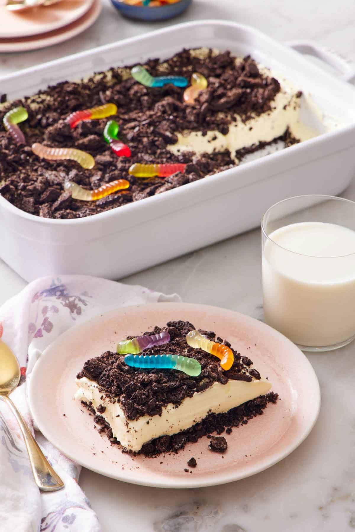 A plate with a slice of dirt cake with a glass of milk and rest of the cake in the background.